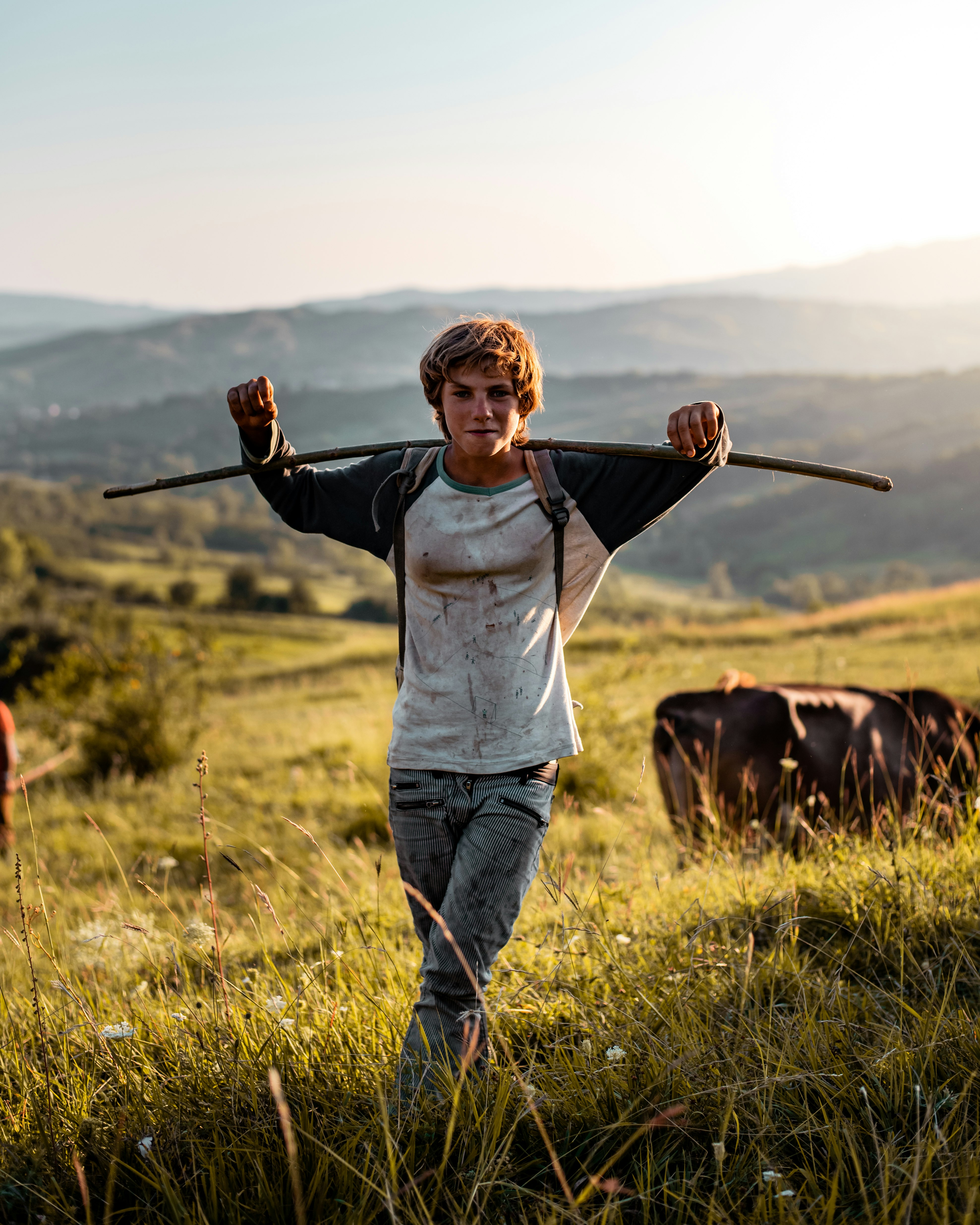 boy in white long sleeve shirt and blue denim jeans standing beside brown horse during daytime